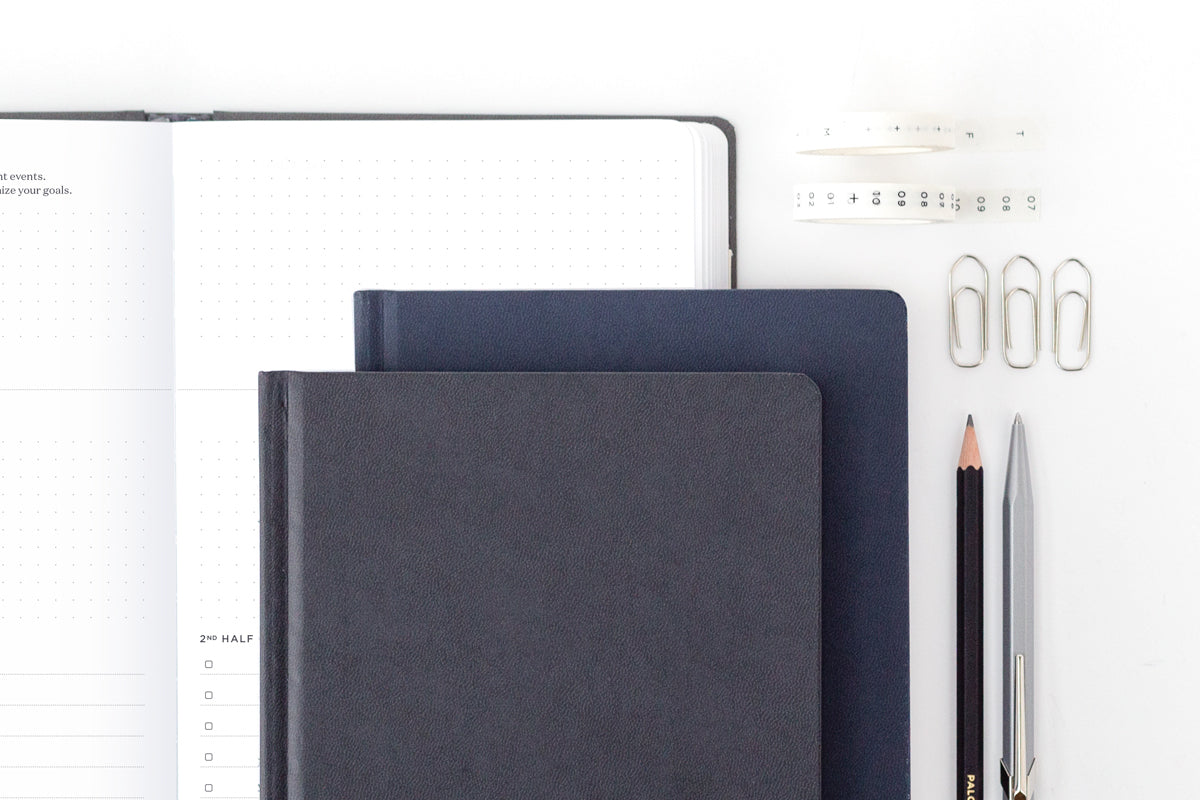An array of customizable productivity tools: a planner, two notebooks, pencils, and paper clips. 