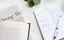 A Today pad is filled out with a to-do list next to a book and a magazine on a marble countertop.