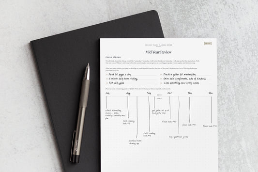 A mid year review check in worksheet on a black planner with a silver pen.