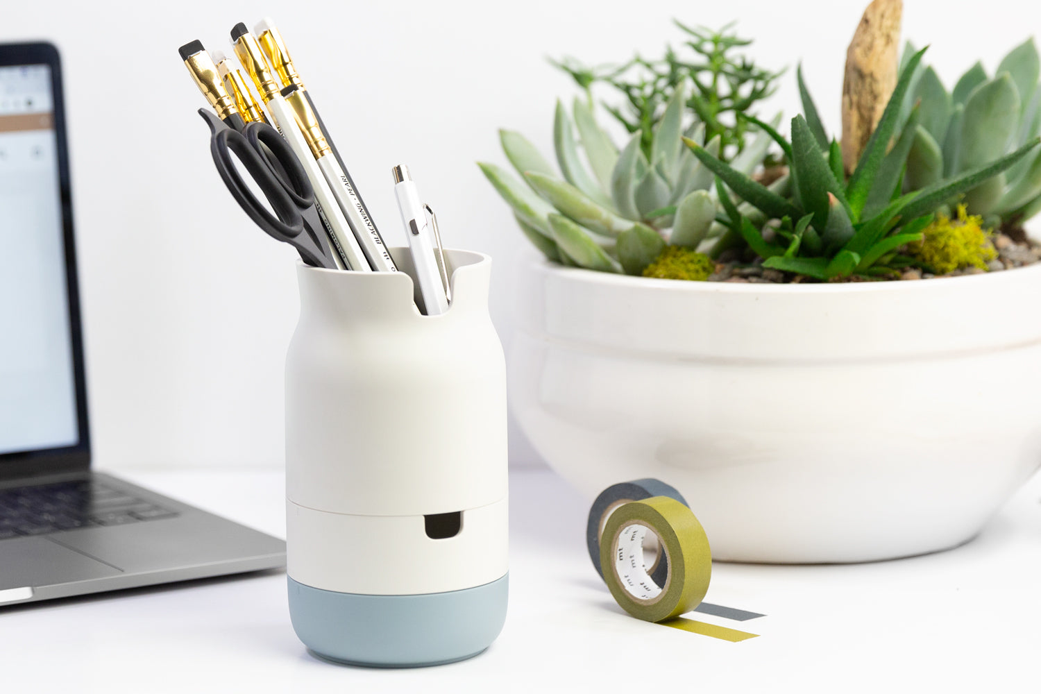 Minimalist office organization supplies, including a white pencil organization cup, white vase, and laptop.