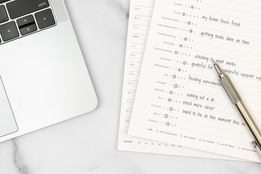 A self-reflection notepad next to a computer on a white table