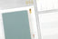 An array of white, gold, light blue planning tools and notepads on a grey desktop.