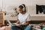 A woman wearing headphones looks at a laptop while sitting on the floor