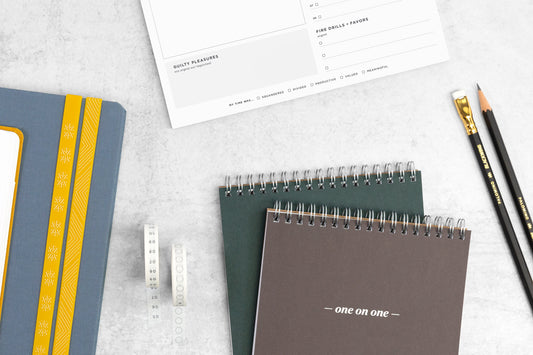 A planner, meeting notepads, and black pencils on a white table.