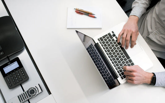 A man sits at a laptop at a white desk.