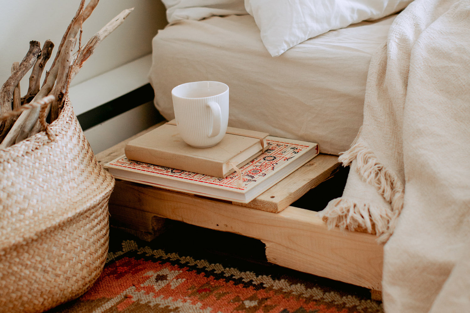 A stack of books under a mug next to a bed