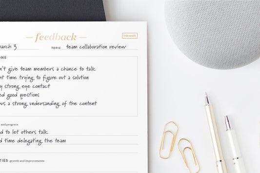 A feedback notepad on a white desk next to a pen and gold paperclips