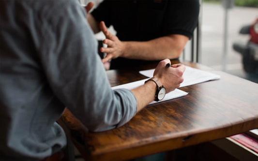 Two men sit at a table, taking notes and having a conversation.