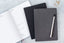 A short stack of three 90 day goal planners, one grey, one black, and one sitting open to a planning page.