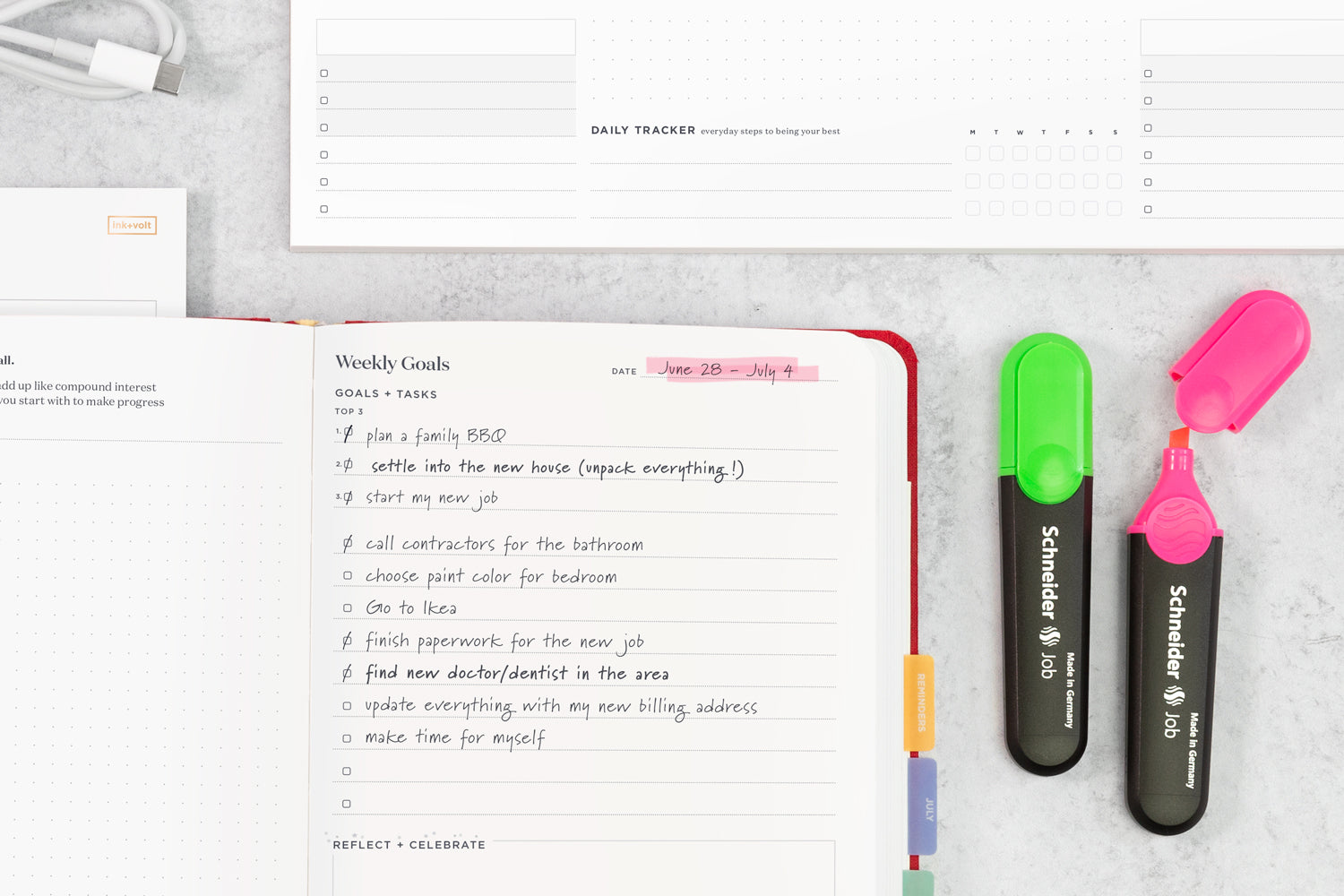 A planner with to-do items listed inside, on a table next to a pink highlighter and a green highlighter.