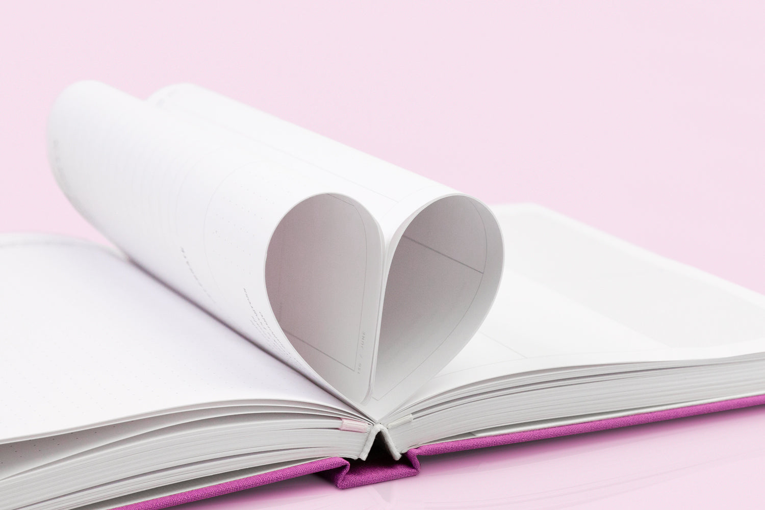 A pink planner is laid open, with two pages tucked together into the shape of a heart.