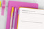 A pink planner open to a "yearly theme" page, on a table next to pink and yellow pens and pink and yellow washi tape.
