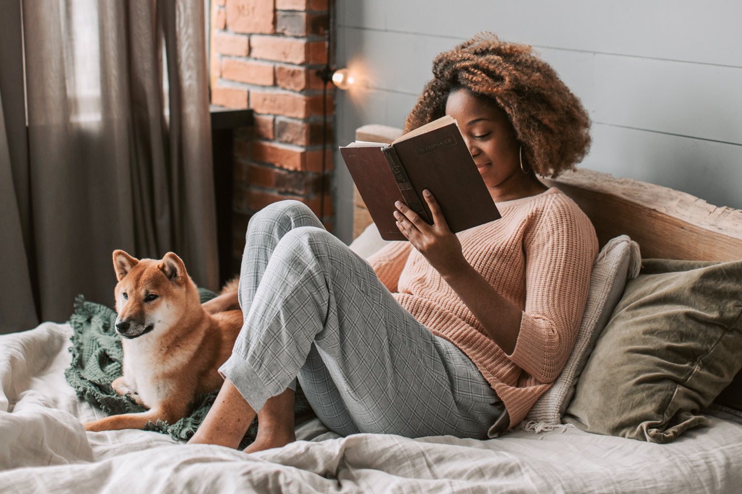 A woman reads a book in bed with a dog
