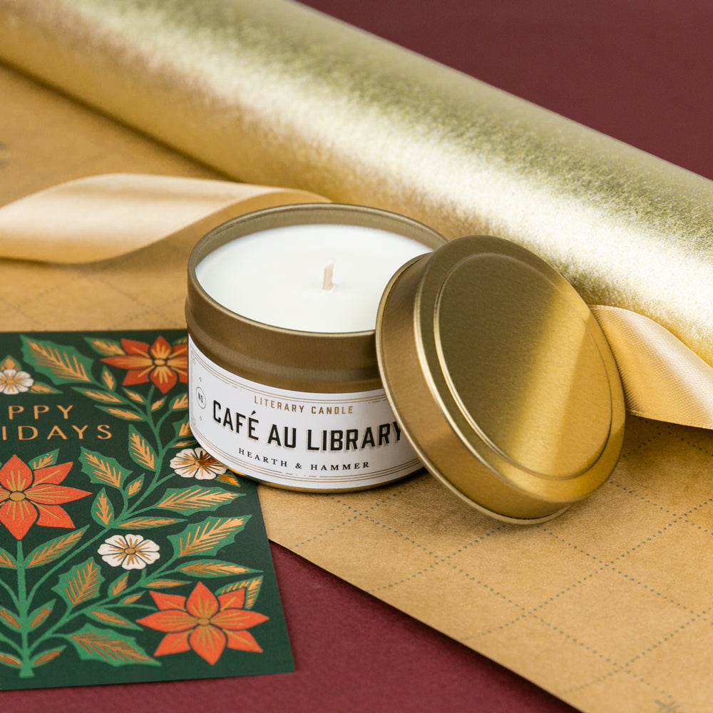 A candle on gold wrapping paper next to a holiday card