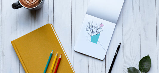 Colored pencils sit on a notebook next to a colored drawing of flowers.