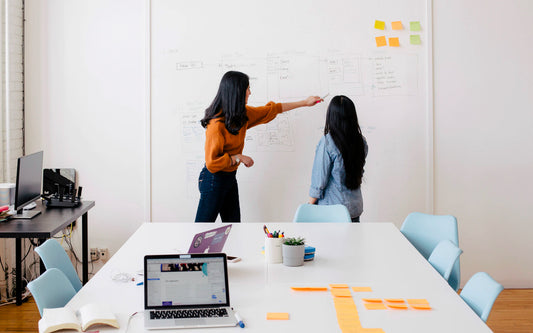 Two women stand in front of a whiteboard in a conference room