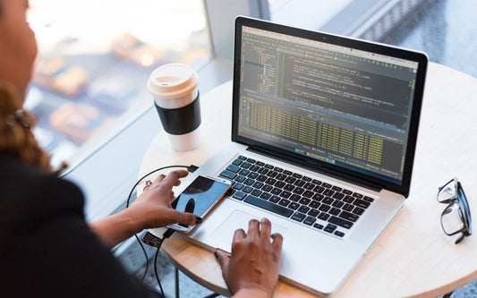 A woman sits at a laptop working on a coding screen.