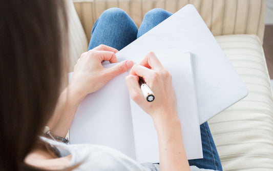 A woman is sitting on a chair writing in a notebook