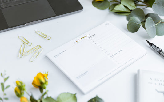 The Ink+Volt Productivity Pad is laying on a desk with gold paperclips and flowers around it