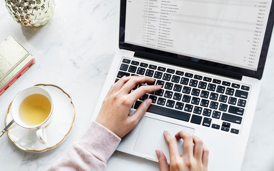 A woman types on a laptop open to her email inbox.