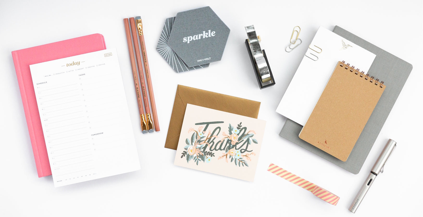 A collection of office accessories: a daily organizer pad, pencils, coasters, thank you cards, paper clips, and pens.