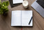 A planner with goals written in it sits on a wood desk next to a green plant, a candle, a laptop, and a blue pen.