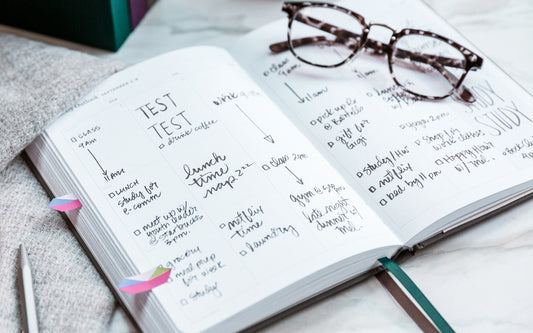 A planner sits open to a page full of writing with a pair of glasses on top of it