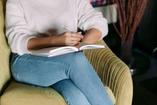 A woman sits in a comfy green chair with a planner open on her lap ready to take notes in a meeting.