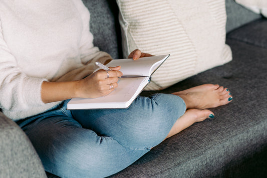 A woman in jeans and a white sweater writes in her yearly planning on a grey couch