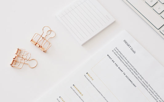 A smart goals template worksheets sits on a white desk next to a computer keyboard and rose gold paper clips.