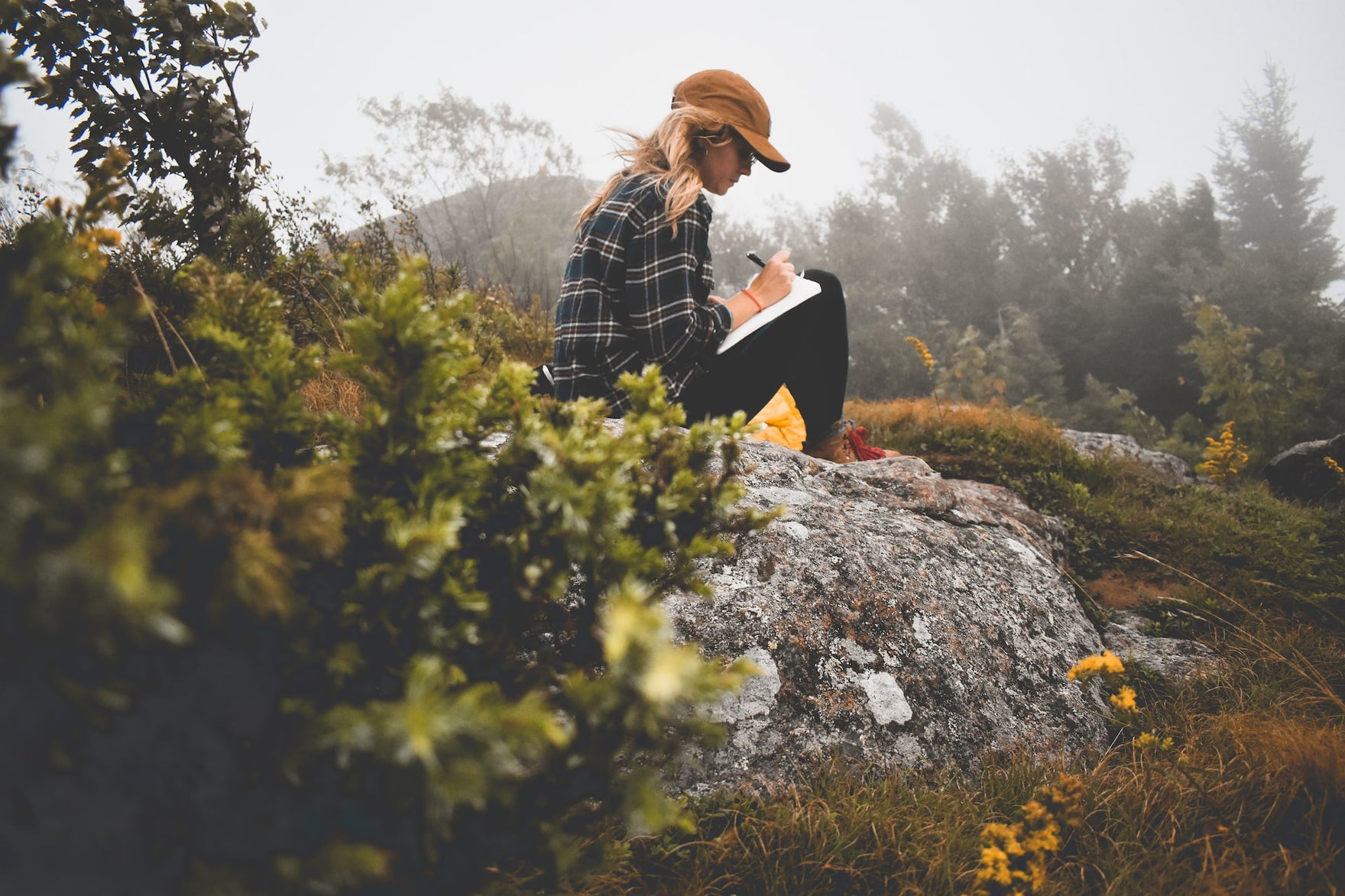 a woman in nature writes in a journal on her lap