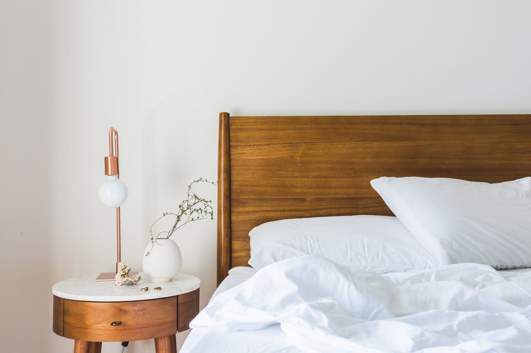A bed with white sheets and a white bedspread is rumpled next to a white and brown wood nightstand