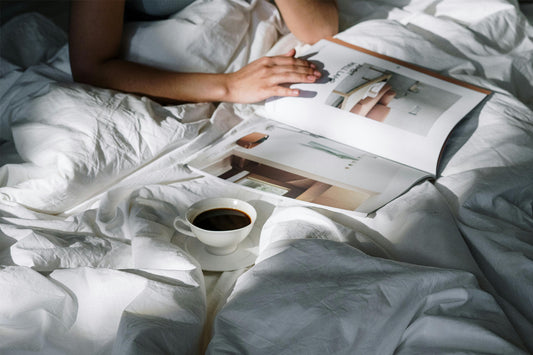 A person reads a magazine in bed with a cup of coffee