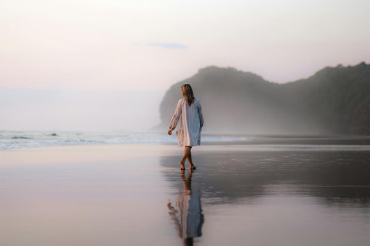 A person in white walks on a misty beach