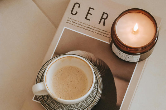 A cup of tea, a candle, and a book on a white table