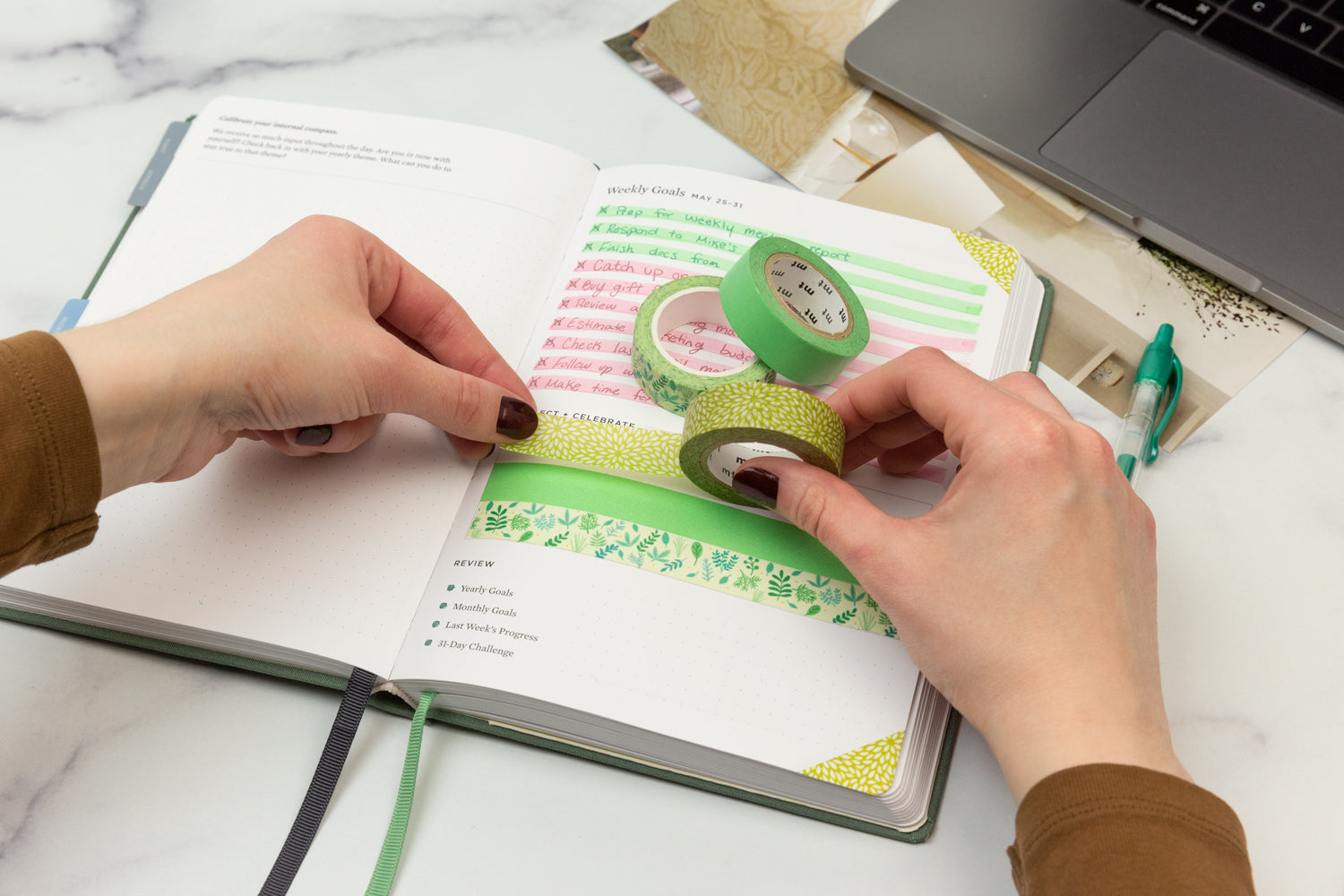 Two hands apply colorful green washi tape to a filled in planner page