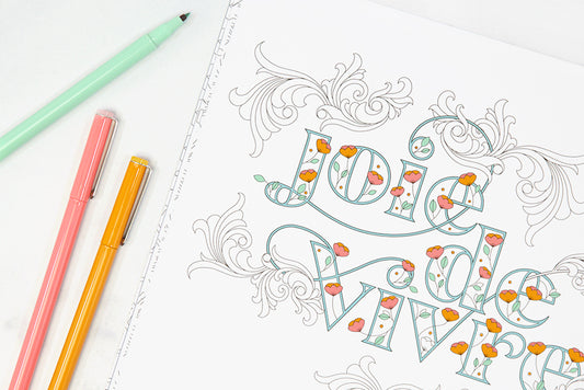 A coloring book page that says "joie de vivre" with colorful markers in green, pink, and gold.