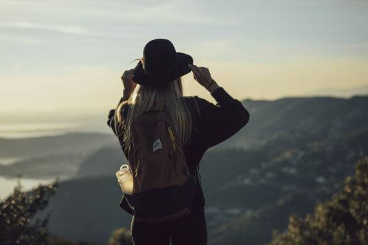 A woman with a hat stands above a view of hills and water