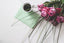 A bouquet of pink roses sits on a table next to a cup of coffee and a sage green envelope.