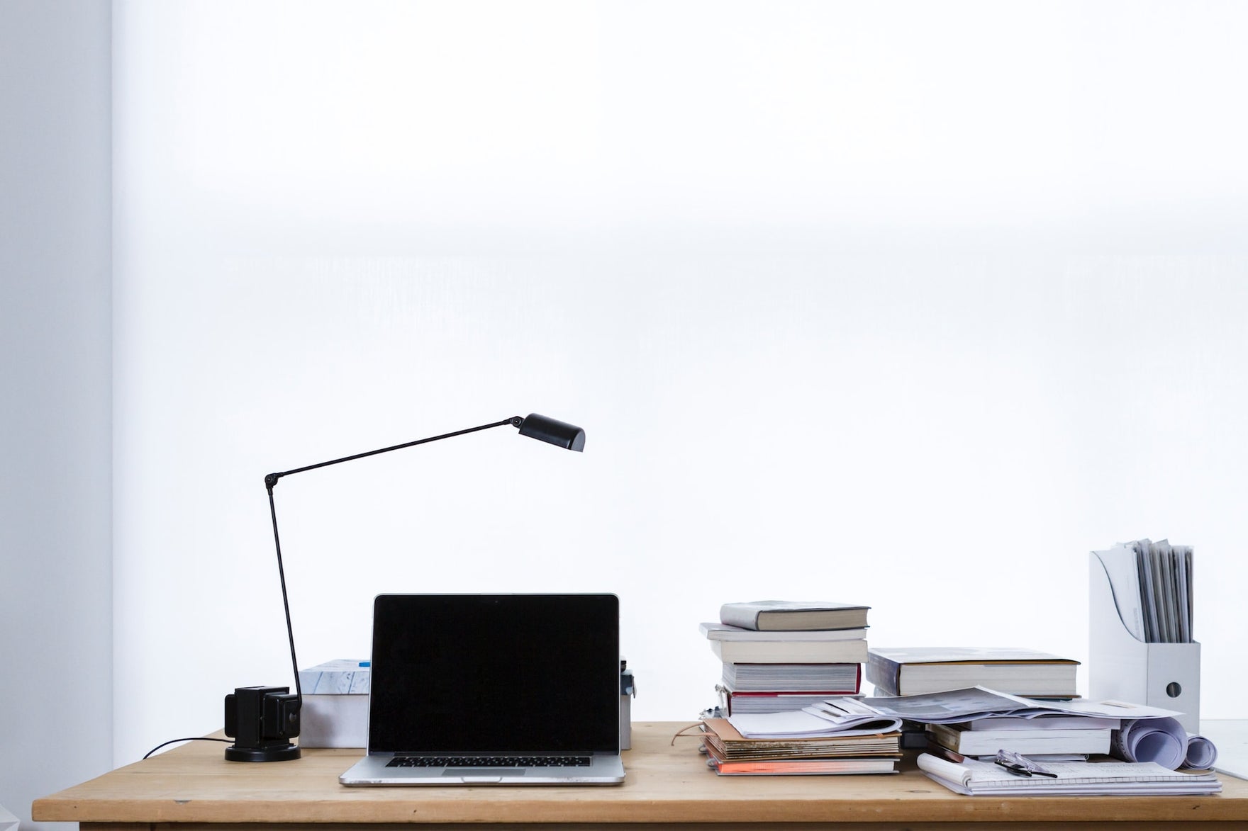 A desk with a computer, a lamp, and a messy stack of books.