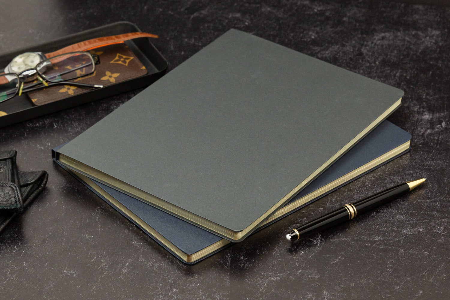 Two fancy notebooks sits on a desk with elegant accessories around them.