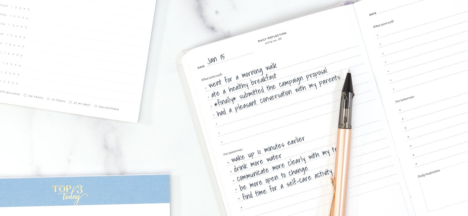 Productivity notepads on a white desk: a top 3 today pad and daily reflection journal
