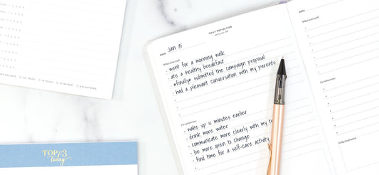 Productivity notepads on a white desk: a top 3 today pad and daily reflection journal