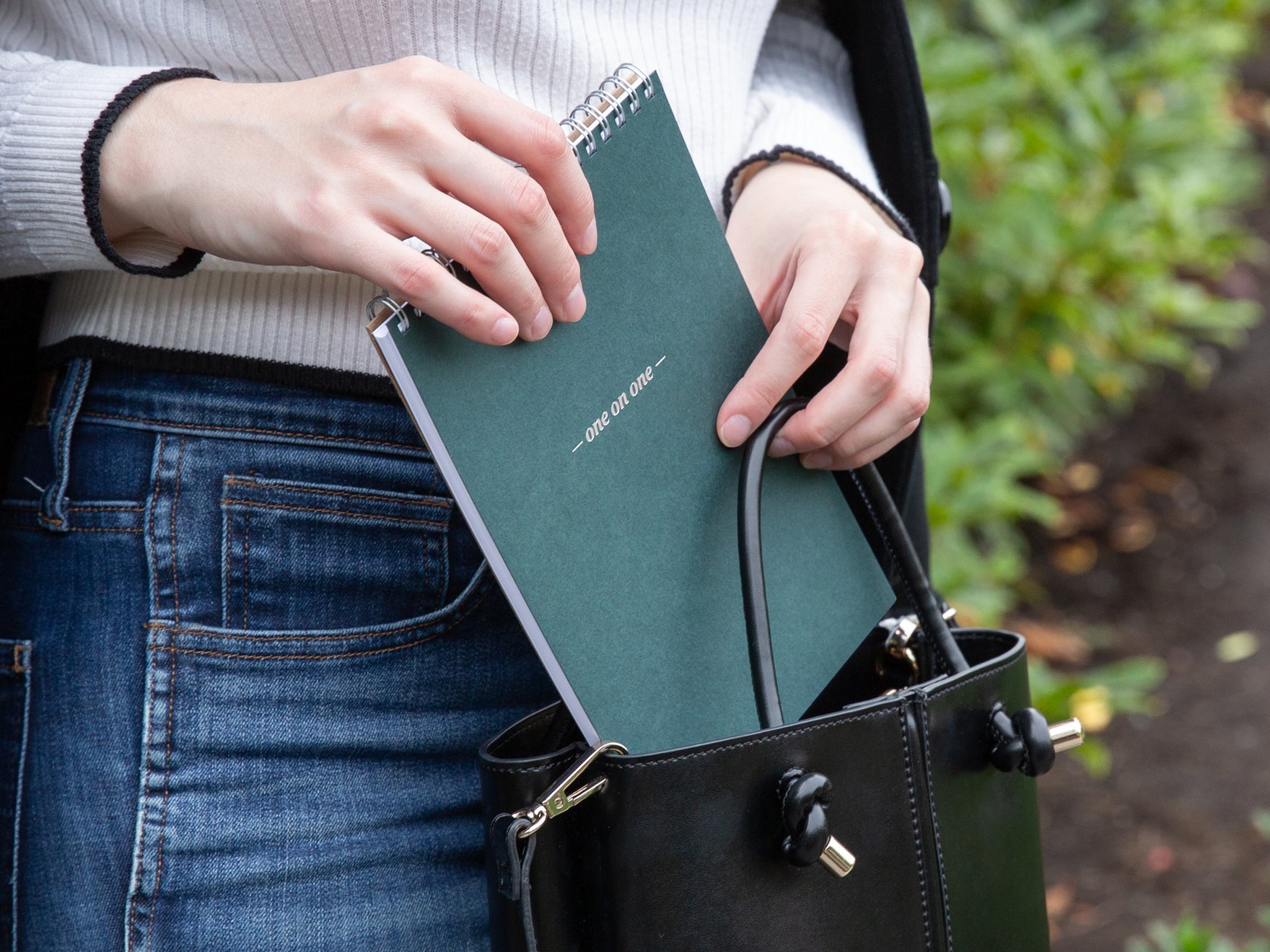 A woman puts a green one-on-one notepad into a black handbag