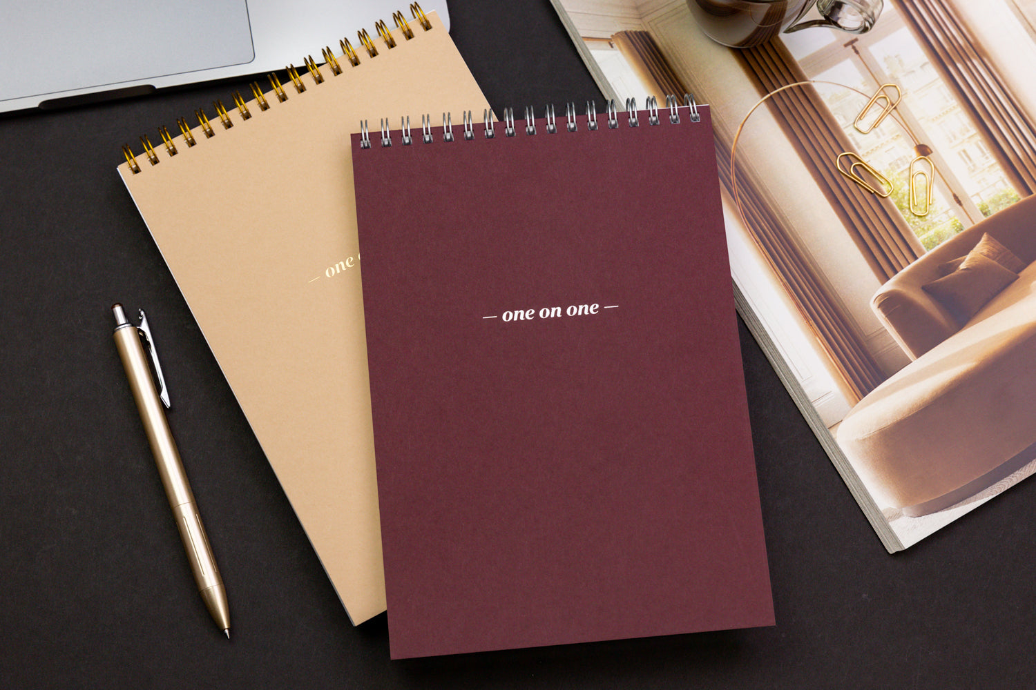 Two spiral one-on-one notepads on a black desk with a gold pen