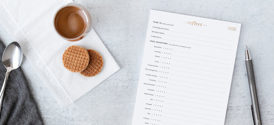 A spoon, cup of tea, two waffle cookies, and a self-reflection notepad