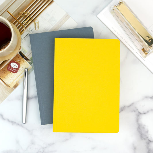 A yellow planner sits on top of a grey planner on a marble tabletop