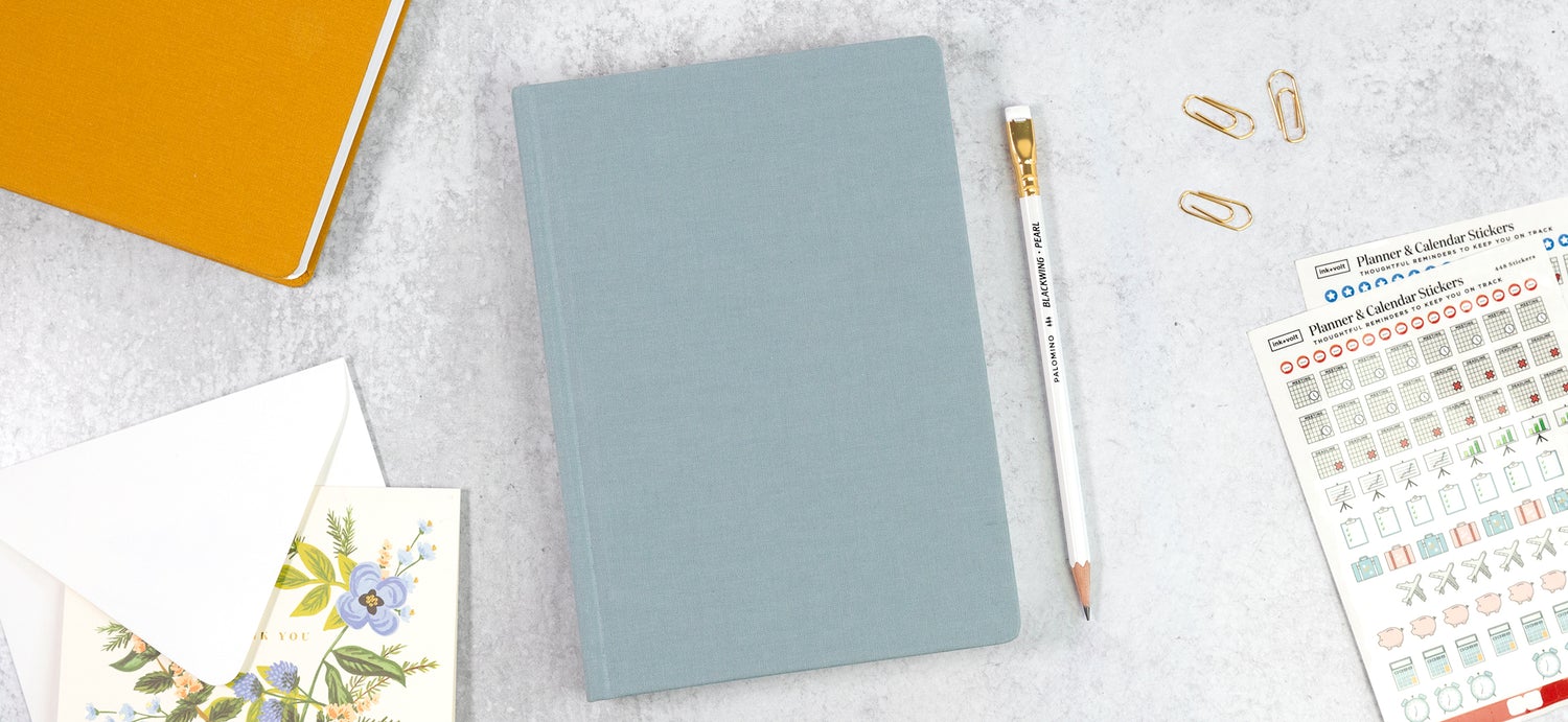 A light blue planner on a white desk with an array of paper accessories.