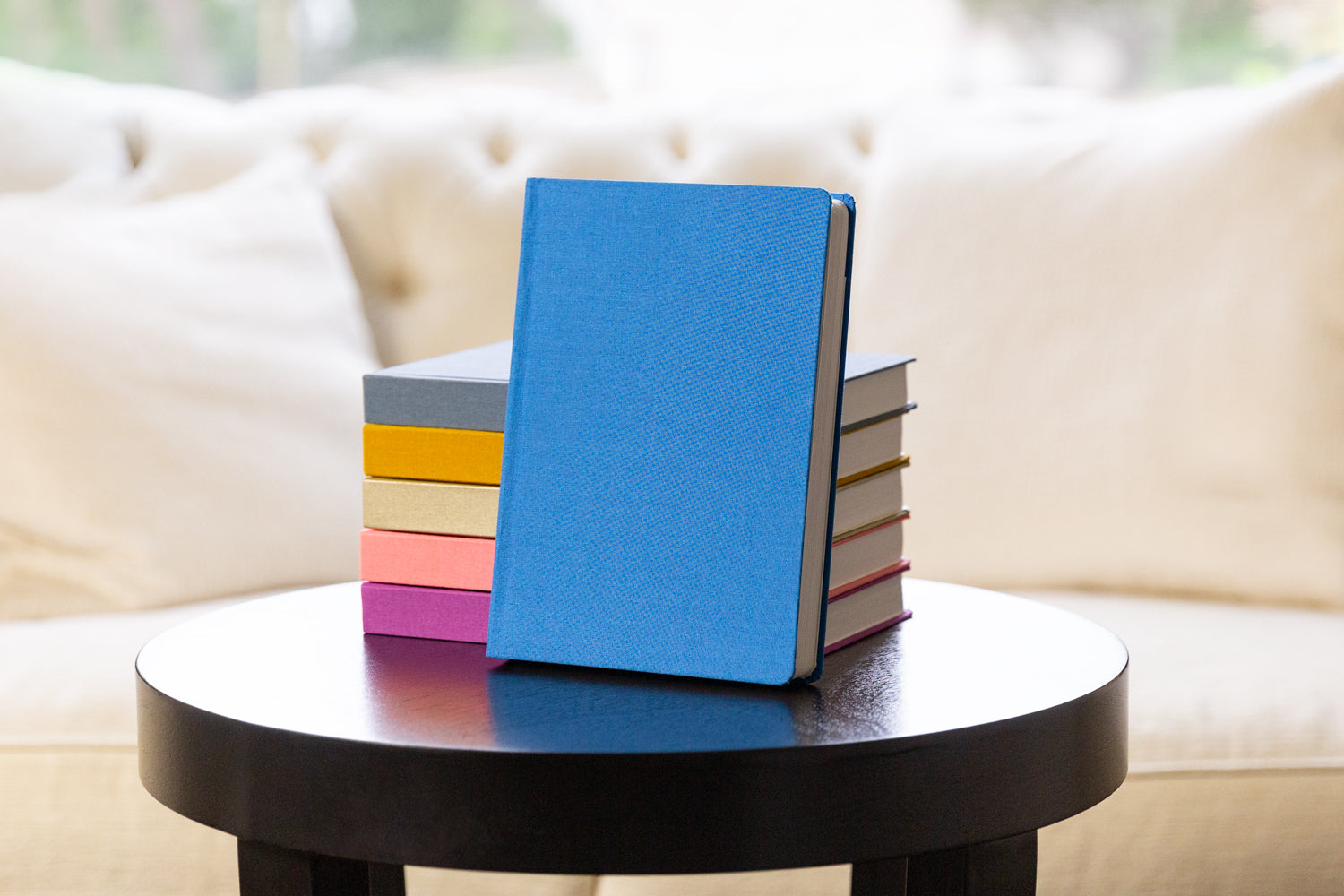 A stack of colorful planners on a dark wood table in front of a white couch
