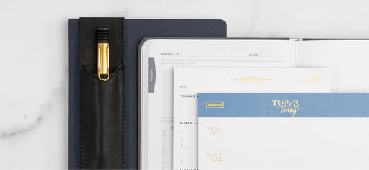 A stack of open planners and notebooks next to an elegant black pen.